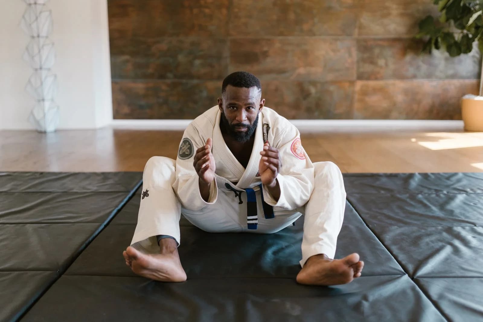 Praticante de kimono sentado no tatame antes de um treino de drill de jiu-jitsu sozinho. Foto de RDNE Stock project via Pexels