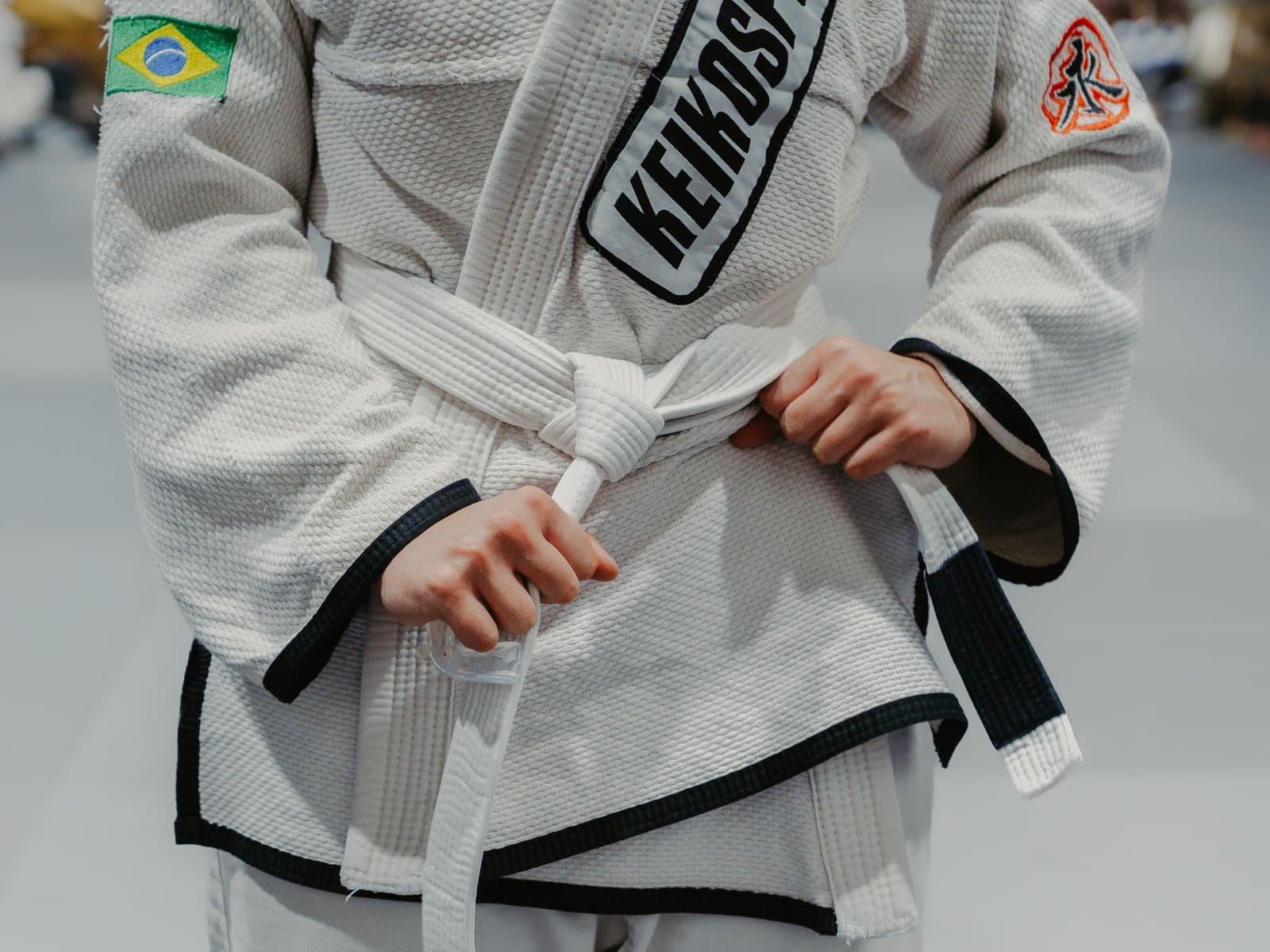 Praticante amarrando a faixa branca de jiu jitsu sobre o kimono antes do treino. Foto de Mica Bassa via Pexels.