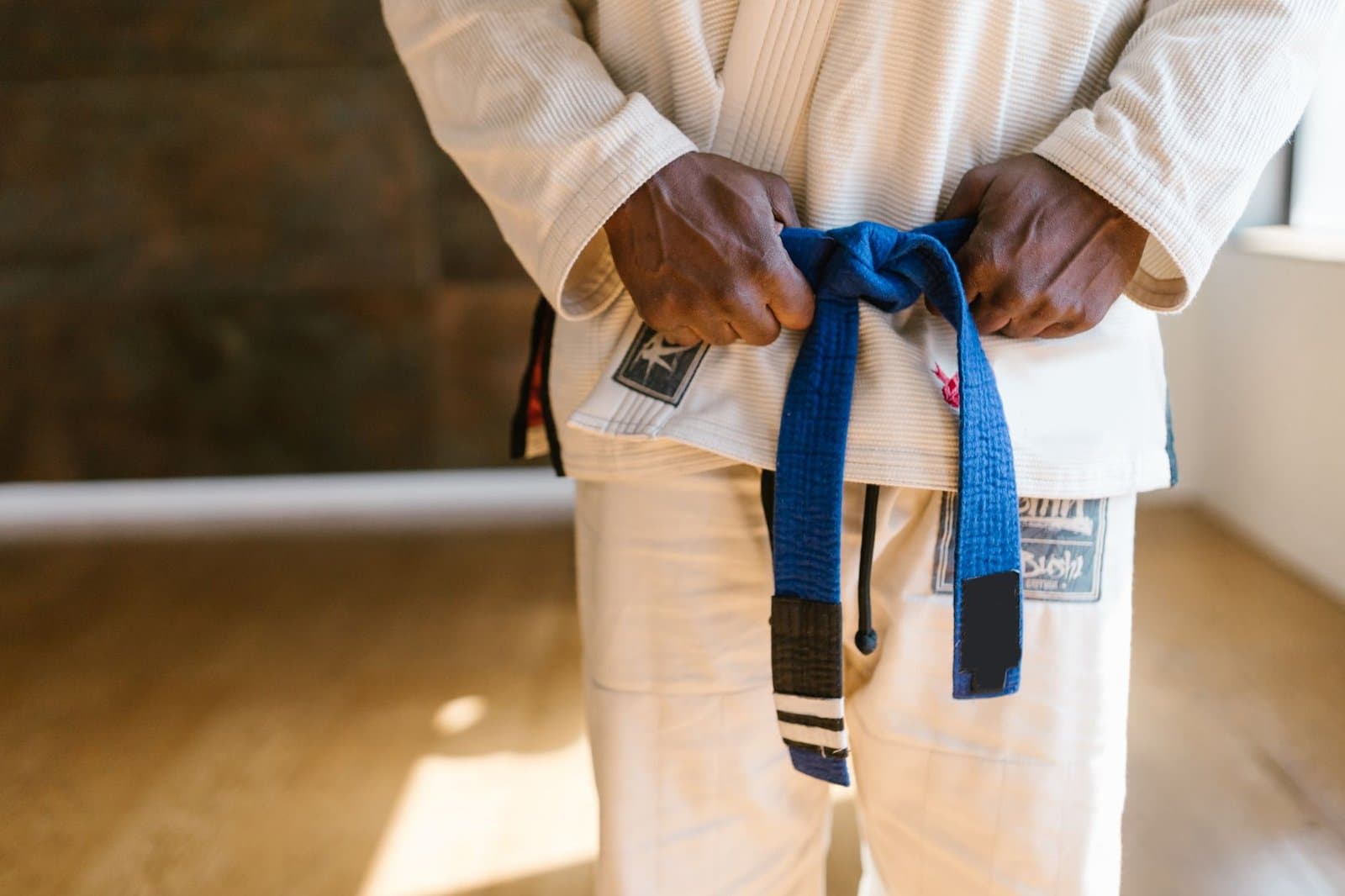 Praticante amarrando a faixa azul de jiu jitsu sobre o kimono branco. Foto de RDNE Stock project via Pexels.