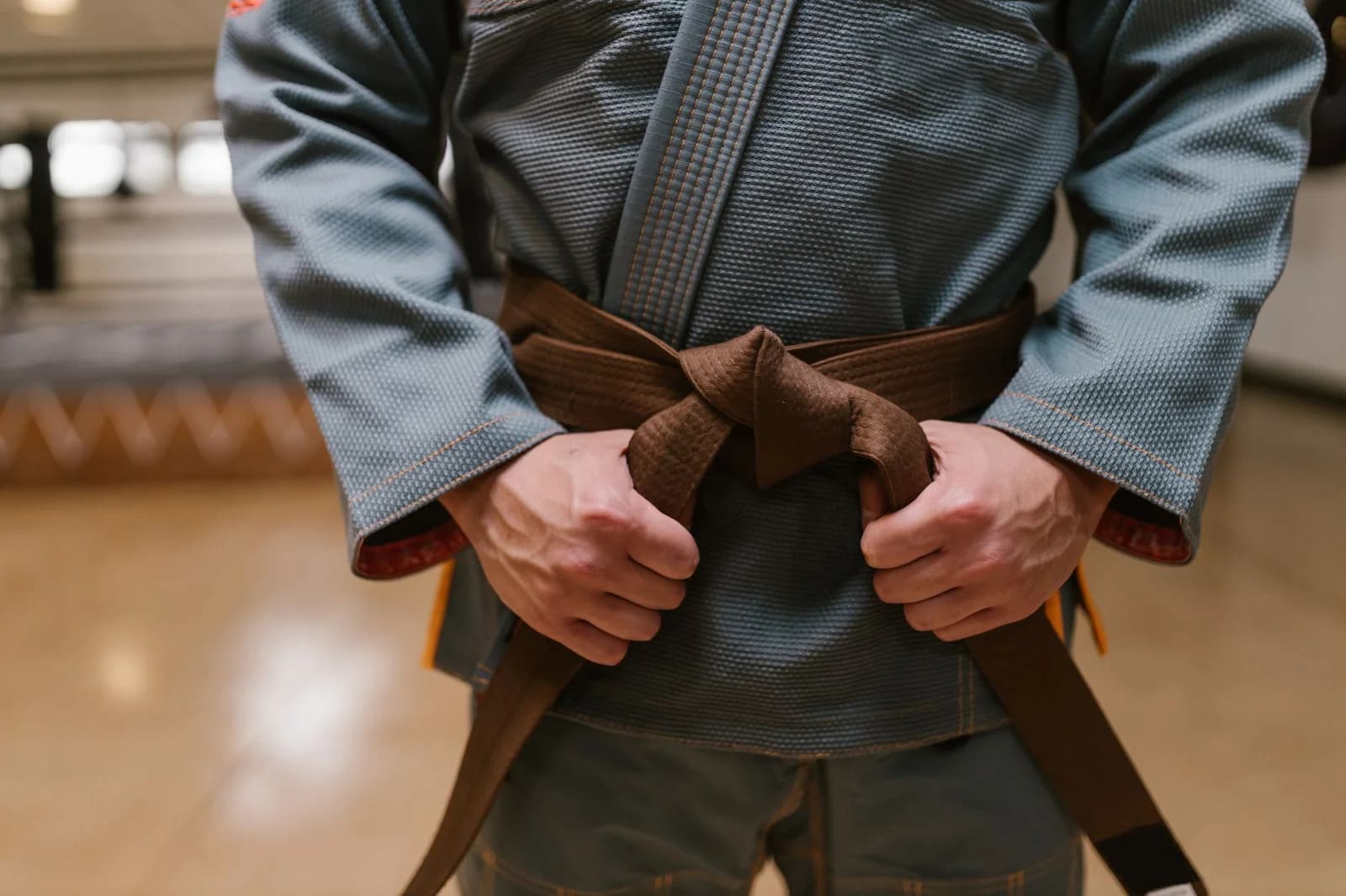 Praticante amarrando a faixa marrom sobre o kimono, uma das cinco faixas do sistema adulto do Jiu-Jitsu. Foto de RDNE Stock project via Pexels.